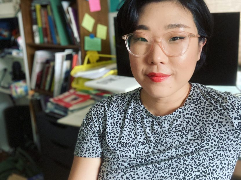 Portrait of Franny Choi sitting in an office with a cluttered desk behind her