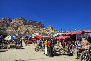 Several red umbrellas at an outdoor market against the backdrop of rugged mountains