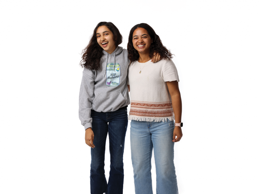 Two students stand together. One student has her arm over the shoulder of the other.