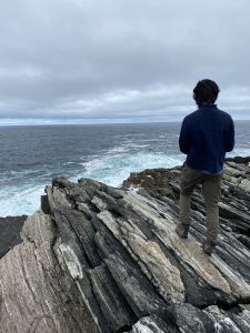 Photo of Nathan Liang standing on a boulder looking out at the sea along Ireland's coastline.