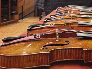 About a half-dozen violins rest side by side on a table in the Brooks Rogers auditorium.