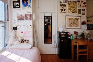 The corner of a dorm room holds a bed and desk and is decorated with posters, artwork and lights.