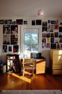 One wall of a college dorm room showing a desk below a large window and walls decorated with magazine pages.