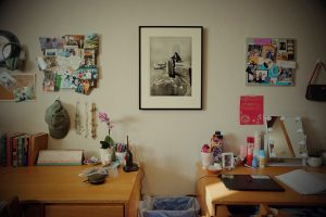 Two desks in a dorm room against a wall decorated with artwork and bulletin boards.