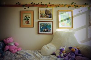 The wall above a dorm room bed is decorated with framed artwork and vines.