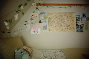 The wall and ceiling above a dorm room bed is decorated with a map, flowers, and posters.