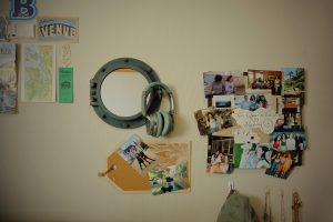 A dorm room wall decorated with a porthole-style mirror and bulletin board of photos.