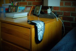 A clock that looks like it is melting over the side of a desk.