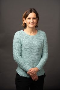 Photo of Esther Duflo, wearing a light blue sweater, hands folded