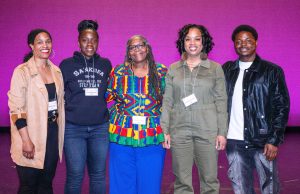 Five people stand together in front of a magenta background.