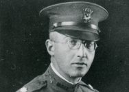 Black and white photo of a man in uniform and round wire-framed glasses