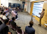 A group of people watching a student make a presentation in front of a screen