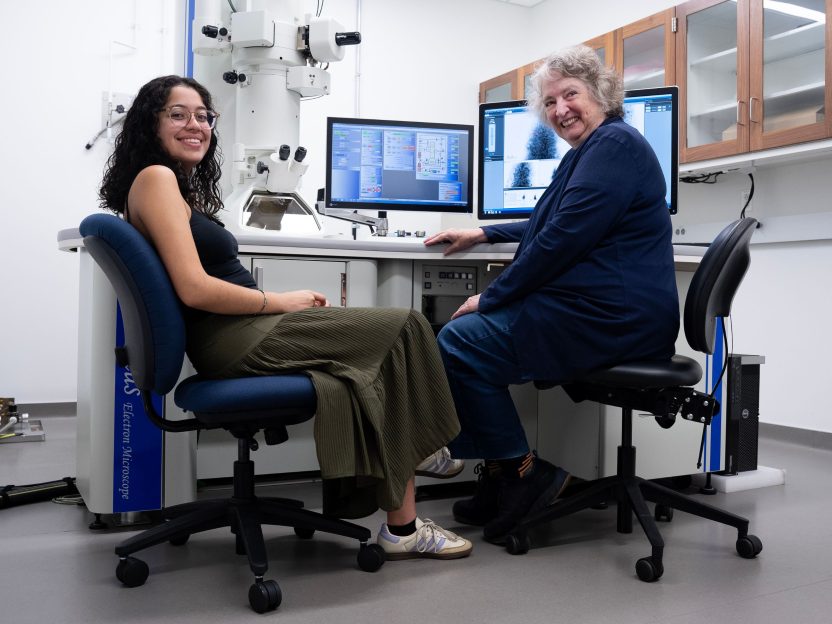 A photo of student Andrea Bustos and electron microscopy technician Nancy Piatczyc seated in from of an electron microscope in the lab.